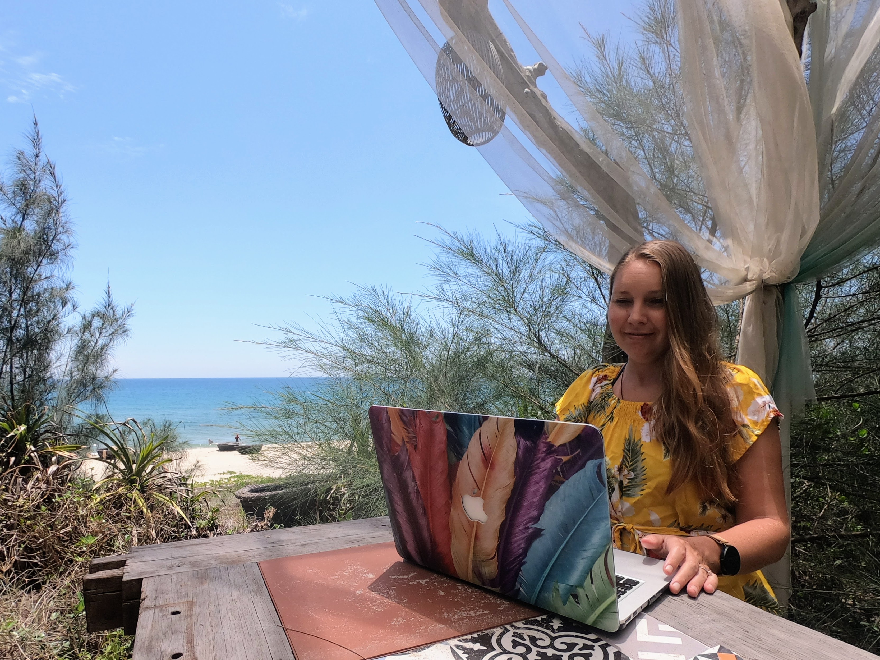 Woman working on laptop outdoors with tropical beach backdrop
